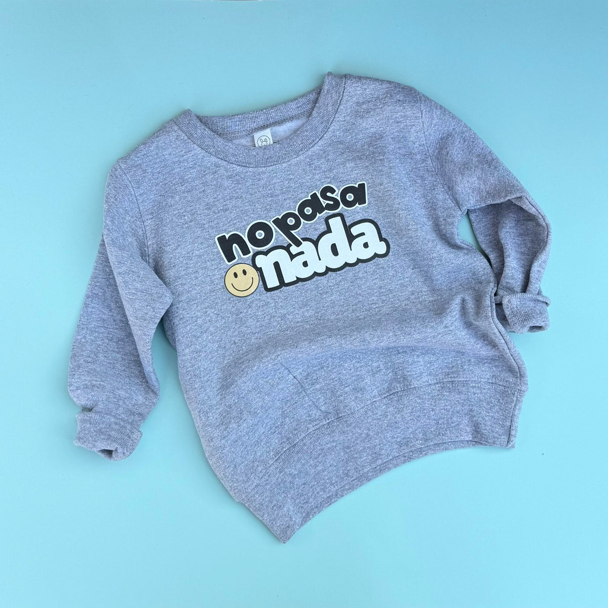 Heathered gray No Pasa Nada kids sweatshirt laid out on blue background